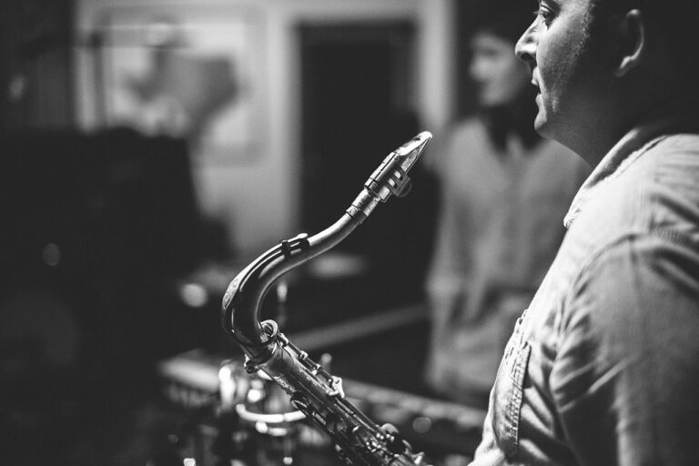 A man plays saxophone in a dimly lit, wood-paneled recording studio.