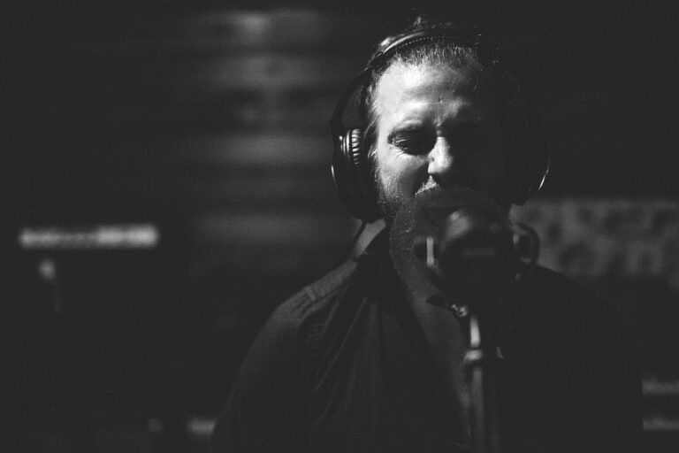A man sings into a microphone in a dimly lit recording studio.